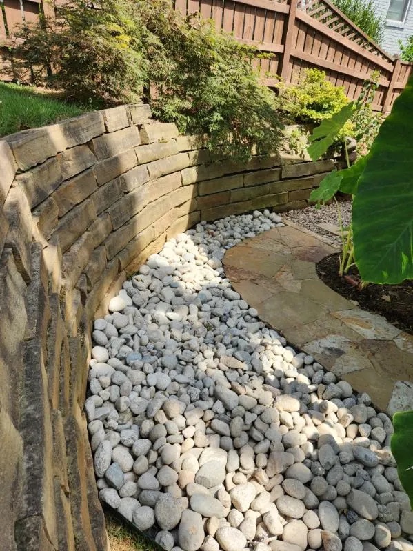 Natural stone retaining wall with white river rock drainage
